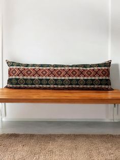 a wooden bench sitting in front of a white wall with a decorative pillow on it