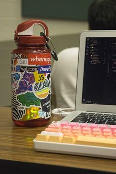 a laptop computer sitting on top of a wooden desk next to a jar filled with stickers