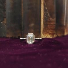 an emerald cut diamond ring sitting on top of a purple velvet covered table next to a book