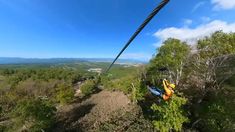 a person on a zip line in the air above trees and land with mountains in the background