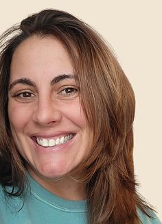 a woman with long brown hair smiling at the camera while wearing a blue shirt and holding a toothbrush in her hand