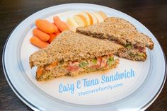 a sandwich cut in half on a plate with carrots and apples next to it