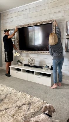 two people standing in front of a flat screen tv on top of a white entertainment center