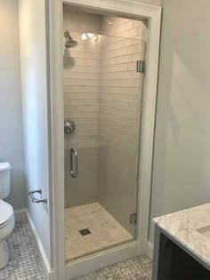 a bathroom with a walk in shower next to a white toilet and sink on a tiled floor