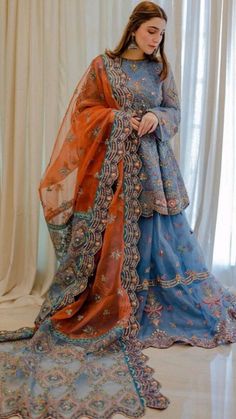 a woman in a blue and orange dress standing on a white floor with curtains behind her