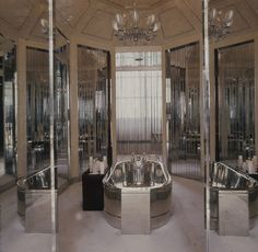 a fancy bathroom with mirrored walls and an oval bathtub in the center, surrounded by glass partitions