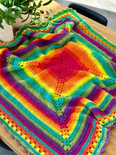 a crocheted blanket sitting on top of a wooden table next to a potted plant