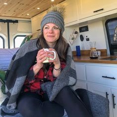 a woman sitting on the floor holding a cup in her hand and smiling at the camera