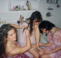 three women in pink robes sitting on a bathtub brushing their hair and looking at the camera