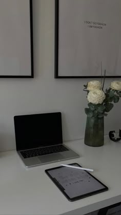 a laptop computer sitting on top of a desk next to a vase with white flowers