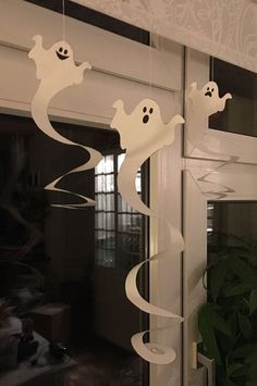 some white ghost decorations hanging from the side of a window in front of a potted plant