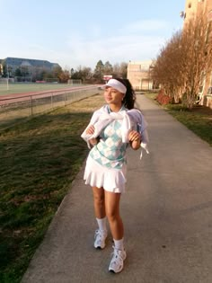 a woman in tennis clothes is walking down the sidewalk