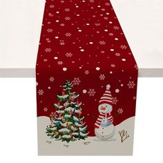 a red table runner with a snowman and christmas tree on it's side