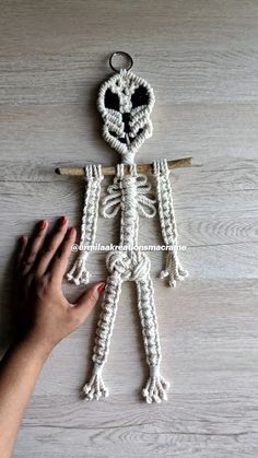 a hand is holding a crocheted skeleton ornament on a wooden surface