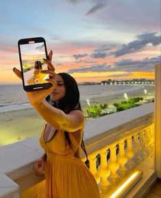 a woman taking a selfie with her cell phone on the balcony overlooking the ocean