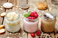 two jars filled with food sitting on top of a wooden table next to sliced bananas and raspberries