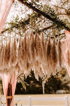 an outdoor wedding ceremony with pink draping and feathers hanging from the tree branch