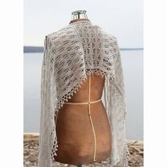 a mannequin wearing a white shawl on top of a wooden table next to the ocean