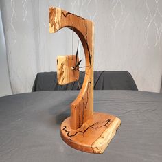 a wooden clock sitting on top of a table next to a gray cloth covered wall