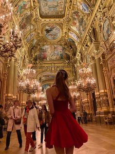 a woman in a red dress is looking up at the ceiling and chandeliers