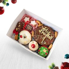 a box filled with assorted decorated cookies on top of a white table next to christmas decorations