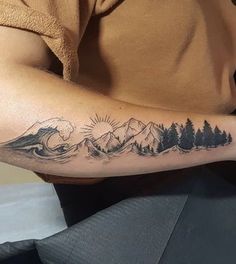 a man with a tattoo on his arm and mountains in the background is holding a cell phone