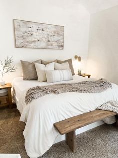 a white bed with pillows and blankets on top of it in a bedroom next to a wooden bench