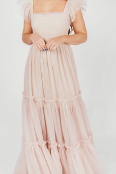 This dress will let your inner princess shine through! Meet the Bella, the dreamy, tulle-layered ballgown we're all obsessing over. This beauty is light as air and destined for the dance floor; from its square neckline and ruffled cap sleeves, to its voluminous multi-tiered tulle skirt, the Bella will capture everyone's attention when you walk in the room. Just don't forget your glass slippers! Available in four colorways. See fabric swatch for true "Peachy Nude" color. FIT: Runs true to size. Y Pink Bridesmaid Dress With Flowy Skirt, Pink Tiered Dress With Voluminous Skirt, Pink Tiered Voluminous Dress, Pink Voluminous Tiered Dress, Elegant Peach Tulle Dresses, Feminine Tiered Maxi Dress For Party, Feminine Tiered Skirt Maxi Dress For Party, Elegant Ruffled Tulle Skirt For Spring, Pink Tiered Skirt Dress For Prom