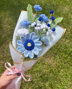 a hand holding a bouquet of blue and white crocheted flowers on top of grass