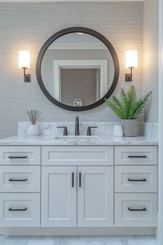 a white bathroom with two sinks and a large round mirror above the sink is surrounded by wall sconces