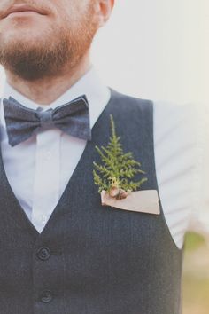 a man wearing a vest and bow tie with a small plant in his lapel