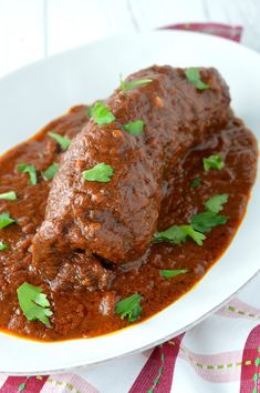 a white plate topped with meat covered in sauce and garnished with cilantro