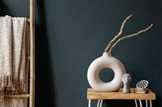 a white vase sitting on top of a wooden table next to a towel rack and ladder