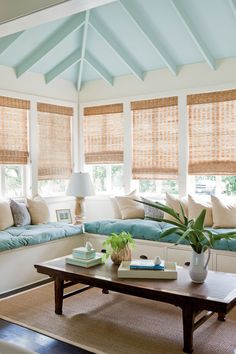 a living room filled with lots of windows covered in blinds and pillows on top of them