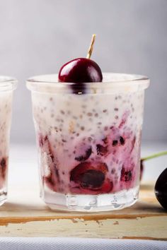 two glasses filled with yogurt and cherries on top of a cutting board