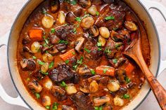 a pot filled with stew and vegetables on top of a table next to a wooden spoon