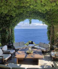 an outdoor seating area with chairs and tables overlooking the ocean in front of a pergolated archway