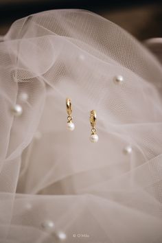 two pairs of earrings with pearls hanging from them on a piece of white tulle