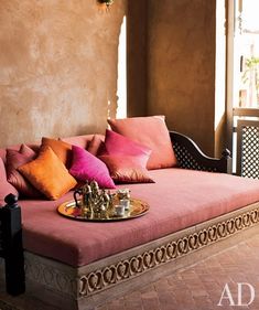 a pink couch sitting on top of a wooden floor next to a window filled with lots of pillows