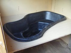 an empty black bathtub sitting on top of a wooden table in a room with unfinished walls