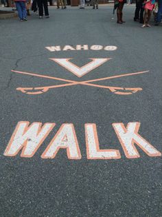 a walk sign painted on the ground with people standing around in the street behind it