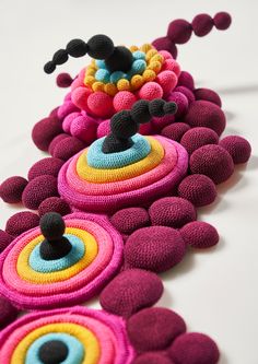 several knitted objects are lined up on a table top, one is multicolored and the other is black