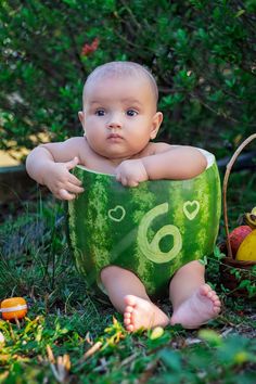 a baby in a watermelon costume sitting on the ground next to some fruit