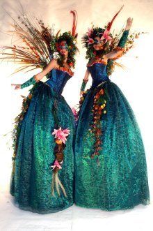 two women dressed in green dresses with flowers and feathers on their heads are standing next to each other