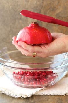 a hand holding an apple over a bowl filled with pomegranates