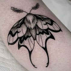 a black and white photo of a butterfly tattoo on the thigh, with leaves coming out of its wings