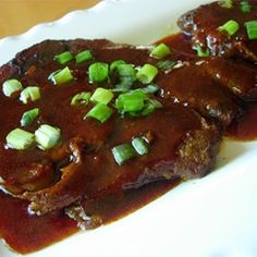 two pieces of meat covered in gravy and green onions on a white plate