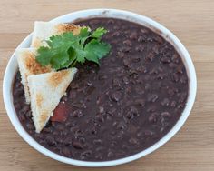 a white bowl filled with black beans and tortilla chips on top of a wooden table