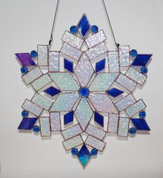 a stained glass snowflake hanging from a hook on a white wall with blue accents