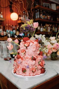 a pink cake sitting on top of a counter next to vases filled with flowers